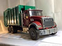 Angled front view of the red and green Bruder Mack garbage truck toy with visible chrome front bumper and detailed grill.
