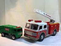 Red and white Tonka Rescue Fire Truck with an extendable ladder next to green Tonka Toughest Minis garbage truck, side angle