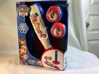 Front view of Paw Patrol soft T-ball set in box showing bat, two baseballs, and tee with packaging graphics.