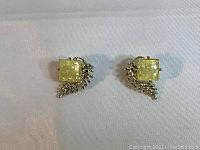 Front view of a pair of clip-on earrings with square yellow amber colored stones and silver-toned branch and leaf accents.