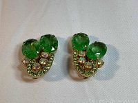 Front view showing two round faceted parakeet green stones accented by clear and light green rhinestones on gold-tone metal clip-on earrings.