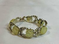 Close-up angled view of the bracelet showing light yellow-green square imitation gemstones surrounded by gold-tone leaf design metalwork.