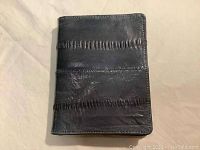 Closed view showing the grey textured eel skin on the trifold wallet.