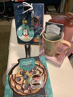 Cast iron skillet with packaging showing pancakes and Nutella, ceramic flamingo mug with hot caramel cocoa, and penguin cookie cutter ornament in gift box with penguin illustration