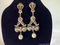 Front view of the pair of chandelier style clip-on earrings featuring detailed ornamental copper design with a pearly bead drop each.