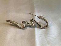 Front view of snake-shaped silver-tone brooch with rhinestone accents on fabric background