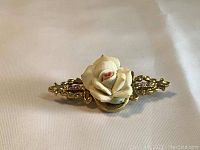 Front view of vintage brooch pin showing glittering golden metal base and ceramic white rose