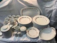 Full set displayed on fabric background including cups, saucers, multiple plates in various sizes, teapot, sugar bowl, creamer, and shakers.