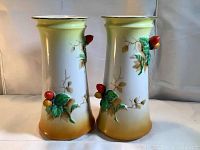 Front view of two matching vintage pottery vases with raised relief red berries and green leaves on brown and beige gradient base.