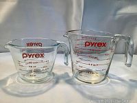 Two Pyrex glass measuring cups side by side, one smaller 1-cup and one larger 2-cup, both with red measurements and handles.