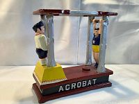 Side view of cast iron acrobat coin bank showing acrobat on bar and standing figure, with 'ACROBAT' painted on base.