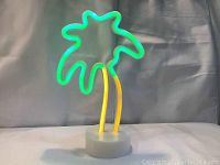 LED palm tree light sign illuminated showing green leaves and yellow trunk on white circular base against a dark background.