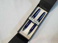 Open box showing dark blue ballpoint pen and mechanical pencil held in place with a white band labeled Pierre Cardin