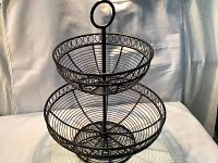 Front and side view of black two-tier wire basket fruit bowl stand with circular handle and loop wire detail around rims