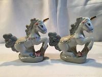 Front and side view of two ceramic unicorn figurines with gold horns and pink rose details