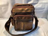 Front view of brown leather shoulder cross bag with multiple zippered compartments and adjustable shoulder strap.