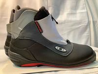 Side profile of one SNS Profil ski boot showing black and gray upper with zippered front cover and logo emblem.