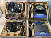 Four Linksys routers by Cisco displayed in their original boxes along with power adapters and Ethernet cables.