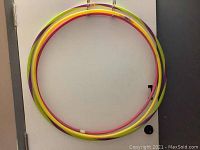 Three hula hoops leaning against a white door showing two smaller hoops stacked on one larger hoop with colorful spiral pattern tubing.