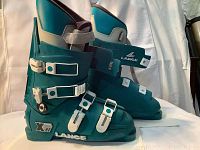 Side view of the pair of teal Lange Xti men's ski boots, showing adjustable white buckles and grey velcro ankle straps.