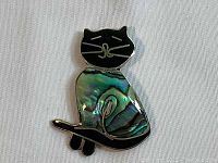 Front view of the cat brooch pin showing black enamel face with gold details and shiny abalone shell body.