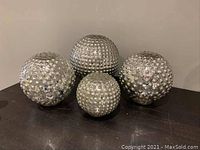 Photo showing a set of four silver mercury glass decorative balls of varying sizes with textured raised dots on their surfaces placed on a dark table.