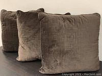 Four brown square throw pillows with velvet-like fabric and geometric embossed pattern, arranged side by side on a flat surface.