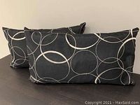 Two rectangular throw pillows placed side by side on a dark surface. Black fabric with white and silver circular swirl designs.