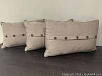 Three brown rectangular throw pillows arranged in a row, showing wood button detailing along the horizontal center line.