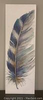 Photo of a 12x36 vertical artwork painting of a large feather in blue, gray, white, and gold on white background.