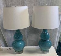 Two teal ceramic table lamps on white surface with fabric backdrop