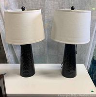 Front view of two identical lamps on a white surface against a sheer curtain backdrop