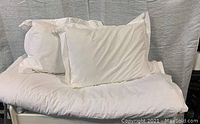 Photo of a white queen duvet cover with 2 matching white pillows and pillow shams arranged on a white surface