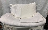 White queen duvet cover laid on table with two white pillows and pillow shams, flat and arranged neatly.