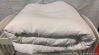 King size white duvet folded and placed on a frame, showing thickness and quilted pattern.