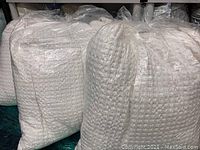 Three large plastic bags containing white Euro sham pillows, packed for sale.