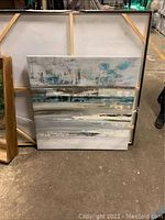 Full front view of the square abstract painting with muted earth tones and teal accents, resting against other large canvases.