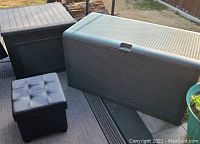 Three storage bins visible including large gray plastic storage bin, brown plastic storage bin with faux wood top, and small black foldable leather-like bin with tufted lid next to a black lattice top plant stand.
