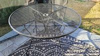 Black iron round patio table with metal mesh top surface and umbrella hole