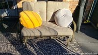 Front view of the patio glider loveseat bench with beige seat and back cushions. Two bean bag pillows in yellow and white are placed on the bench.