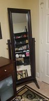Full-length beveled cheval mirror with solid dark wood frame standing beside a door and dresser.