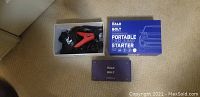 Photo of Halo Bolt portable car jump starter charger and jumper cables in a box on carpet.