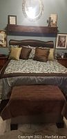 Bed with brown padded headboard, decorative pillows and footstool
