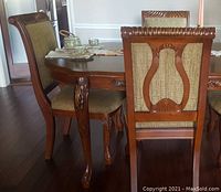 Four upholstered side chairs around a dining table, showing harp back design, upholstered seat and back, carved detailing on crest and legs, and horse hoof front legs