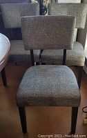 Three dining chairs with button-tufted backs and brown gold striated upholstery arranged near dining table