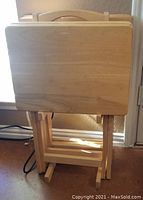 Image showing all five snack tables stacked together in folded position, highlighting their natural beechwood finish and compact stacking design with handle on top for transport.