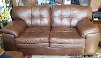 Front view of brown leather loveseat showing tufted seat and back cushions, loose seat cushions, armrests and walnut stained wood block feet.