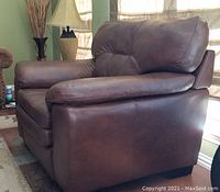 Three-quarter side view of brown leather armchair showing tufted back, plush arms and hardwood block feet