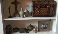 Full view of white shelf showing wood and cane accented chest, stoneware turtle figurine, pottery, wooden cross, candle holders, and scripture plaque.