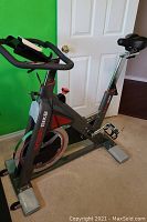 Full side view of the gray and red steel frame showing spin flywheel, pedals with toe cages, resistance knob and adjustable seat post